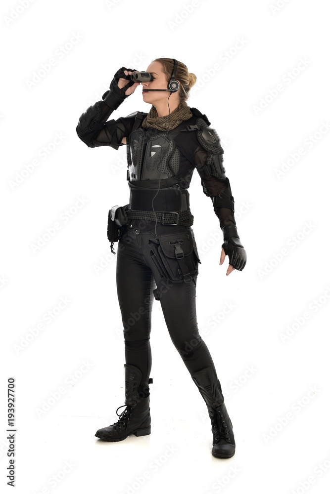 full length portrait of female  soldier wearing black  tactical armour  holding  a pair of binoculars, isolated on white studio background.