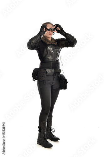 full length portrait of female  soldier wearing black  tactical armour  holding  a pair of binoculars  isolated on white studio background.