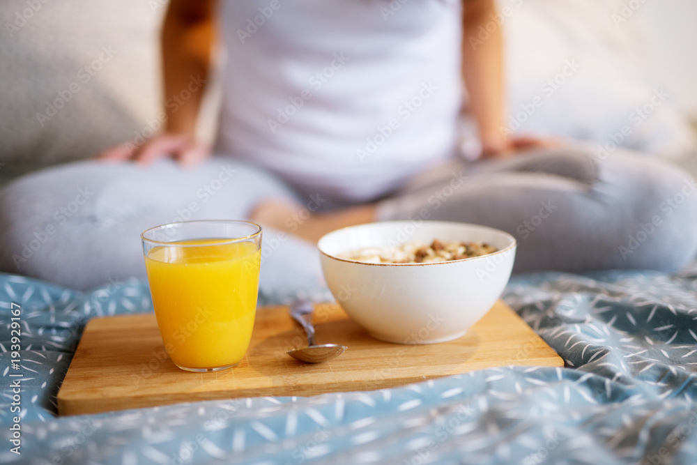 Close up of woman sitting on bed, with breakfast and juice on wood in front of her..