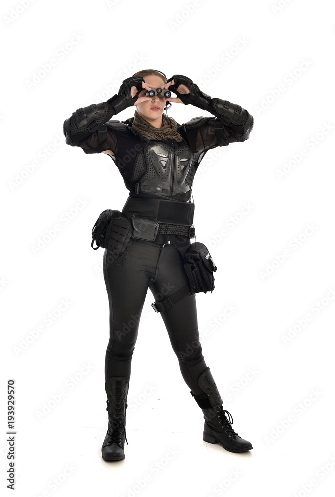 full length portrait of female  soldier wearing black  tactical armour  holding  a pair of binoculars, isolated on white studio background.