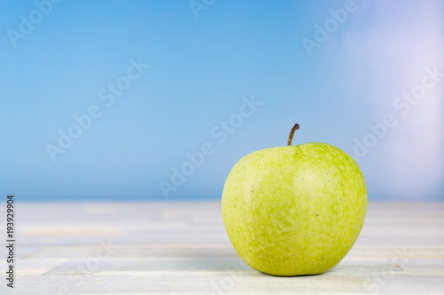 Green apple on wooden table, blue sky background