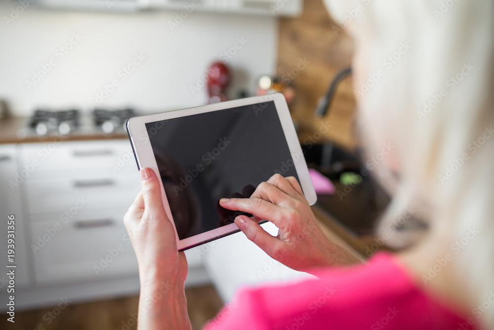 Senior lady standing at kitchen using tablet