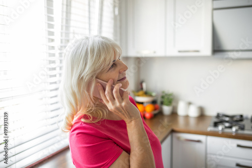 Happy senior lady talking on mobile in kitchen