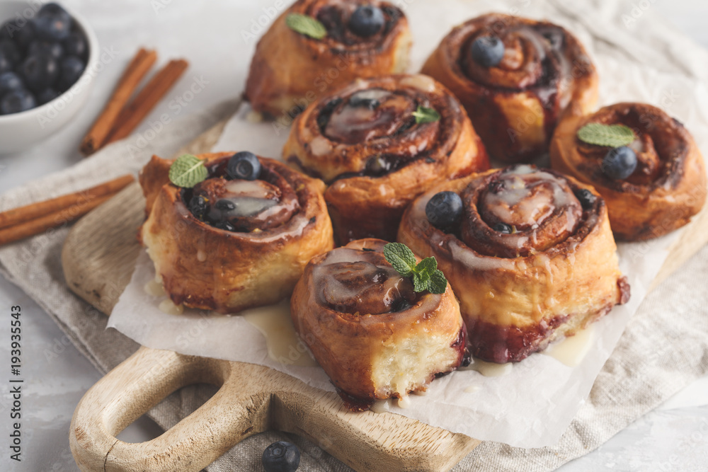 Homemade cinnamon buns with blueberries and cinnamon on a white wooden board