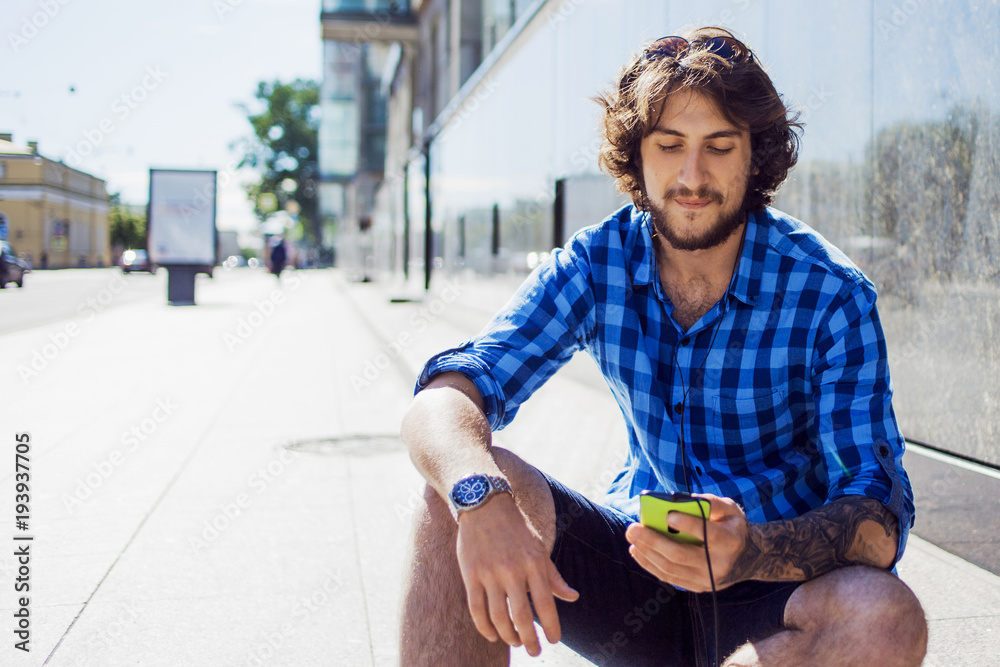 Bearded guy choose the music track in mobile app.. Portrait of young handsome stylish man on the street.