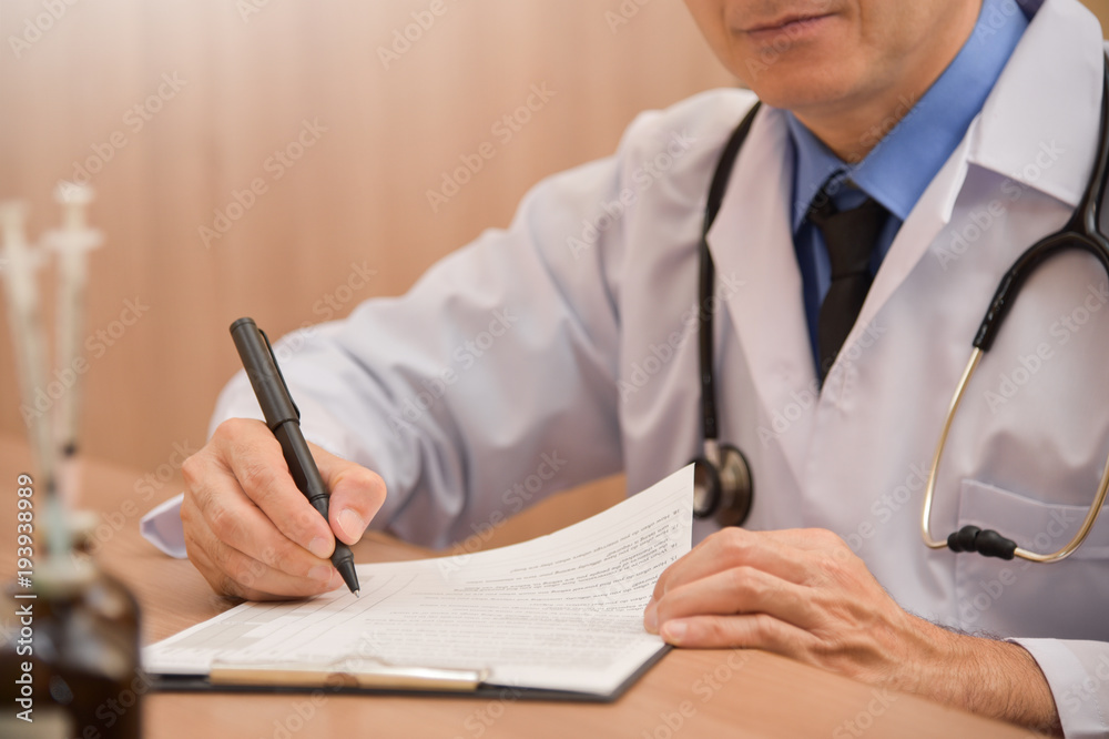 Asian male doctor is writing something on clipboard. Asian male doctor is writing something on clipboard.