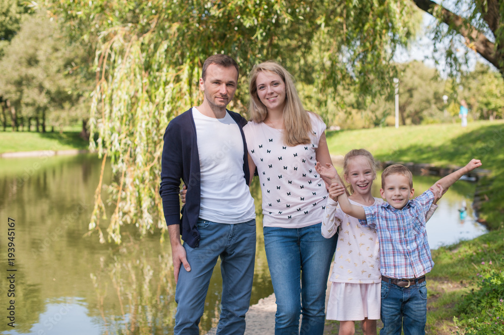 Fototapeta premium Mom and dad playing with their handsome son and daughter - Family and children outdoors in the park - Young beautiful family posing for the photographer