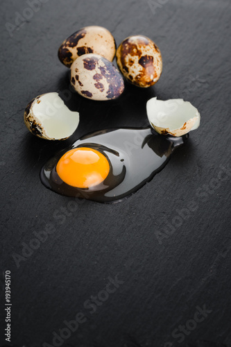 Quail eggs on black stone background, broken, cracked quail egg, yolk of quail egg. Organic product.