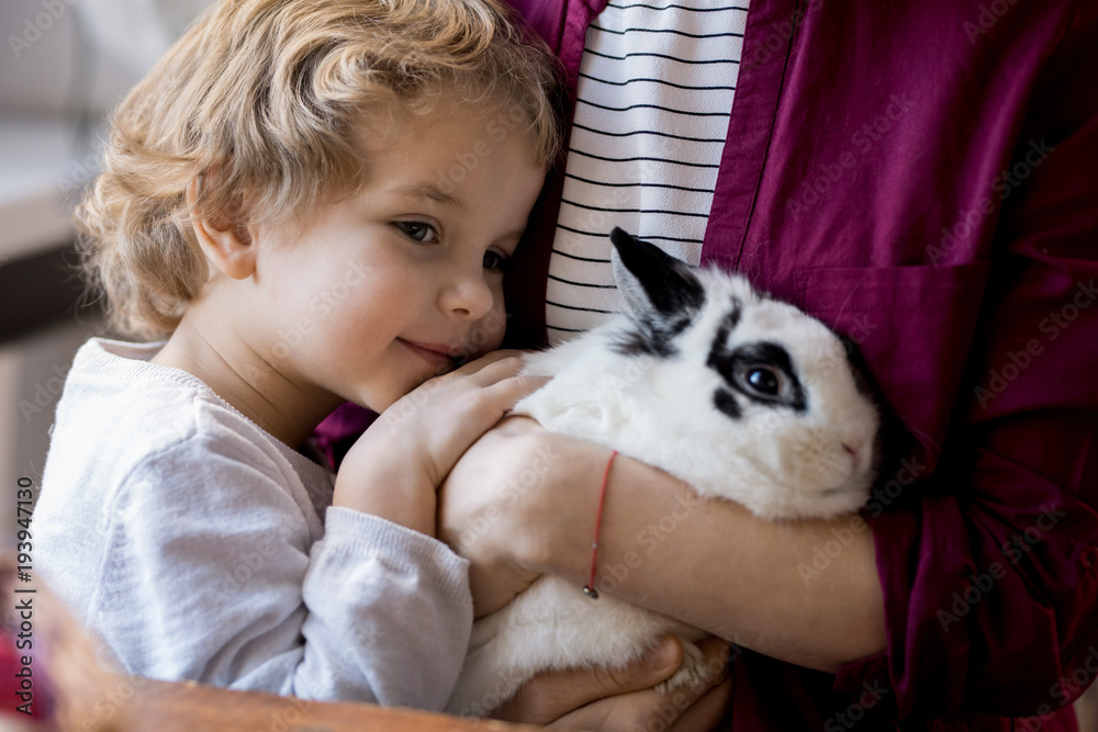 Fototapeta premium Close up portrait of cute blond toddler hugging pet bunny and clinging to mom