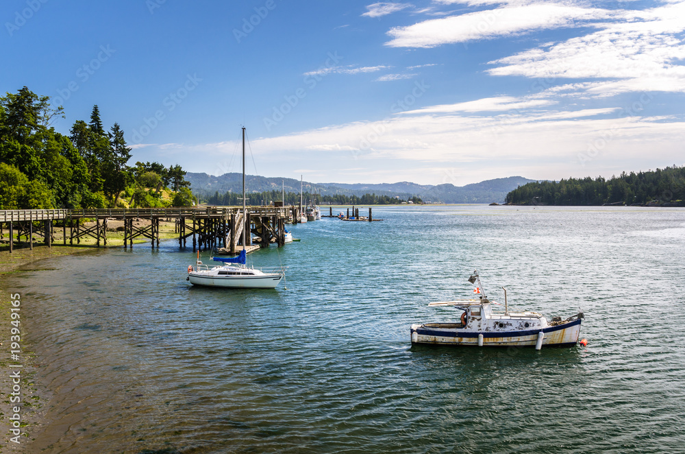 Two Anchored Boats with Wooden Piers in Background in Sooke Harbour on a Summer Morning.