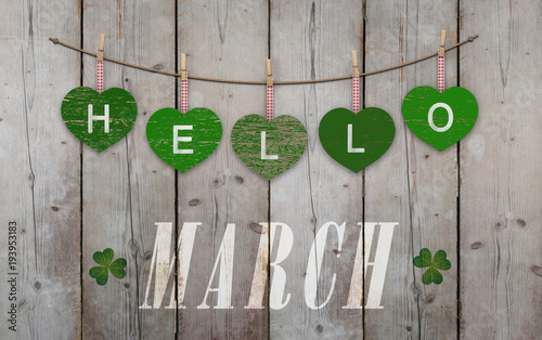 Hello March written on hanging green hearts and weathered wooden background, with clover photo