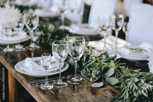 Decorated elegant wooden wedding table in rustic style with eucalyptus and flowers, porcelain plates, glasses, napkins and cutlery
