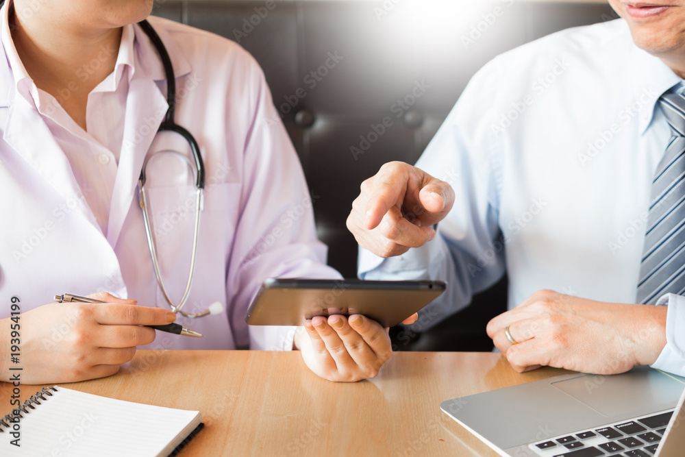 Two doctors discussing patient notes in an office pointing to a tablet as they make a diagnosis or decide on treatment Two doctors discussing patient notes in an office pointing to a tablet as they make a diagnosis or decide on treatment