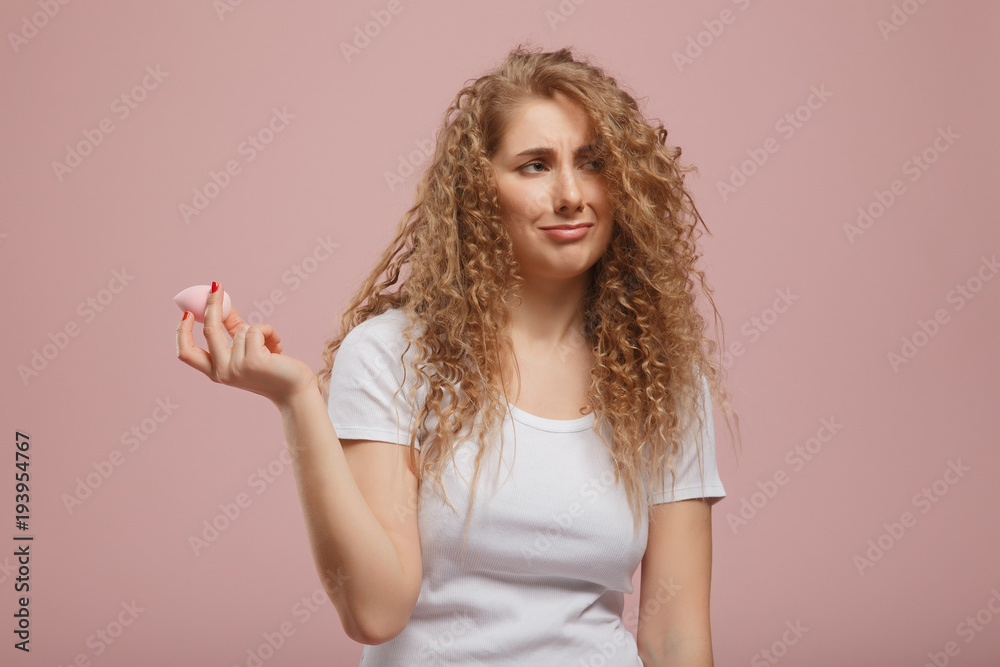 Beauty blender. Beautiful girl with curly hair with makeup sponge in hands looking into camera. Concept of doing make-up on your own home