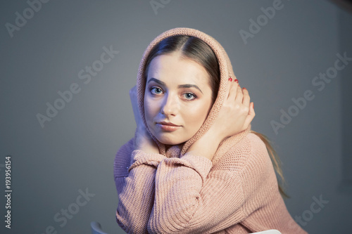 large emotional portrait of a beautiful girl in a knitted pink headscarf in the studio on a gray background.