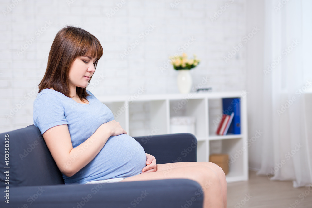 beautiful pregnant woman sitting on sofa in living room and looking at her belly beautiful pregnant woman sitting on sofa in living room and looking at her belly