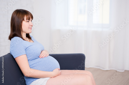 young beautiful pregnant woman sitting on sofa and holding her belly in living room