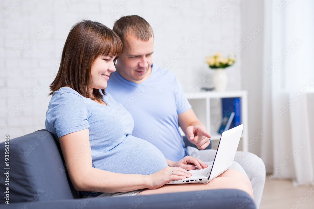 online shopping concept - pregnant woman and her husband using laptop in living room online shopping concept - pregnant woman and her husband using laptop in living room
