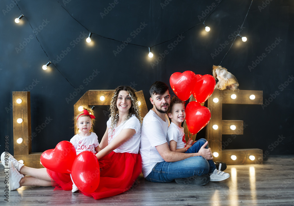 Beautiful young family and their little kids pose with balloons in a cosy studio. Studio family portrait.