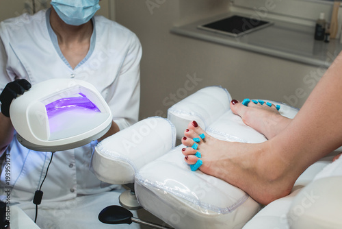 Pedicure foot and nails treatment with cosmetic products and UV lamp photo