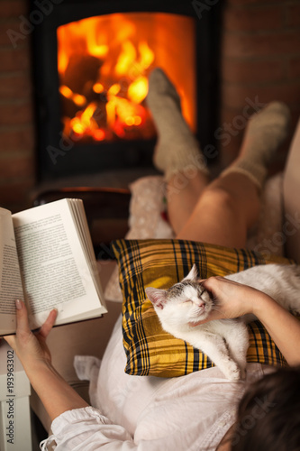 Woman relaxing at the fireplace with a book and her kitten