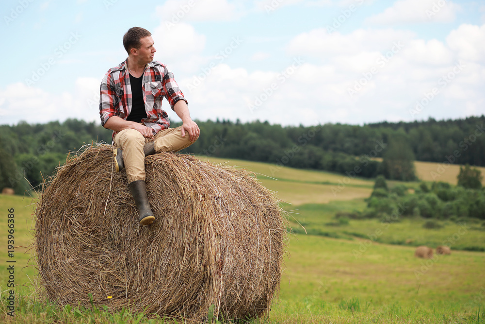 Young man in boots in village field at sunset Young man in boots in village field at sunset