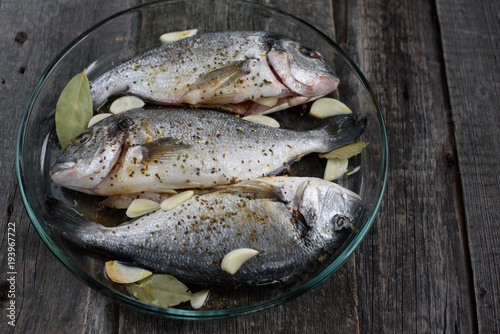 Dorado fish on a glass dish for baking, wooden background