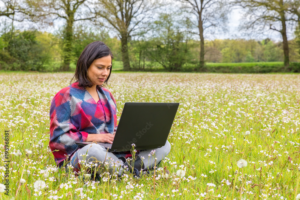 Woman sitting with laptop in blooming meadow Woman sitting with laptop in blooming meadow