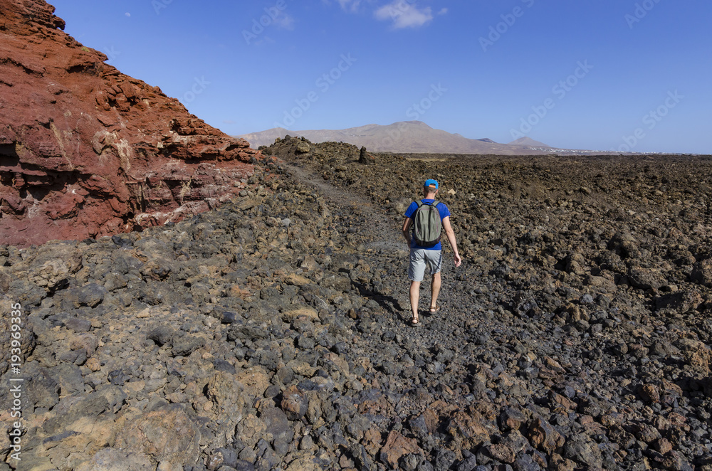 A man with a backpack trekking along a rocky route in volcanic landscape of Timanfaya National Park on Lanzarote, the Canary Islands