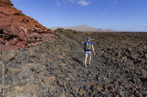 A man with a backpack trekking along a rocky route in volcanic landscape of Timanfaya National Park on Lanzarote, the Canary Islands