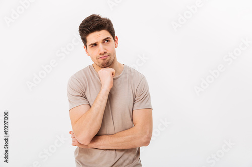 Photo of pensive man propping up chin and posing aside with serious look, isolated over white background