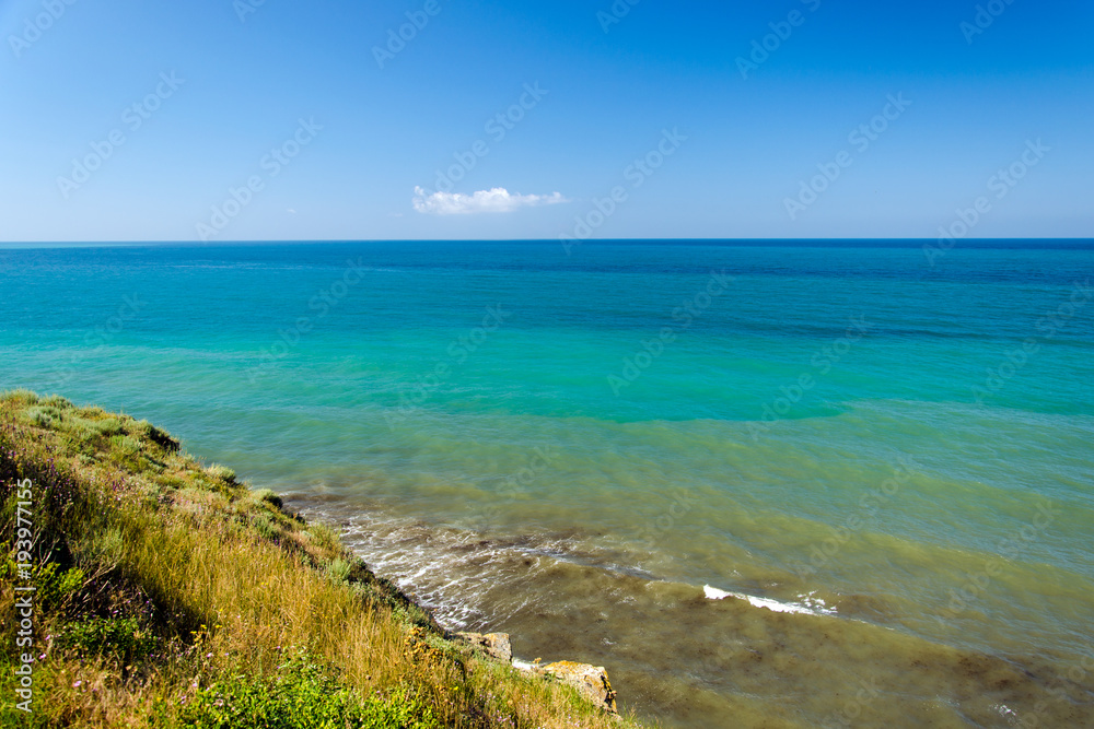 Black Sea seascape with waves at steep bank. Brown, green and blue waves and blue sky above sea.