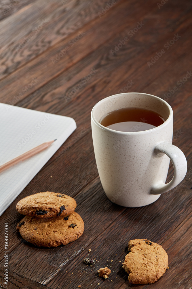 Cup of tea with cookies, workbook and a pencil on a wooden background, top view Cup of tea with cookies, workbook and a pencil on a wooden background, top view