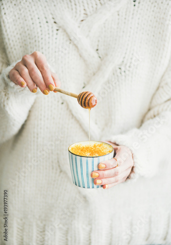 Healthy vegan Ayutvedic hot drink. Female in white loose sweater holding cup of turmeric latte or golden diary-free milk with honey in hands. Clean eating, alkaline diet, immunity boosting concept photo
