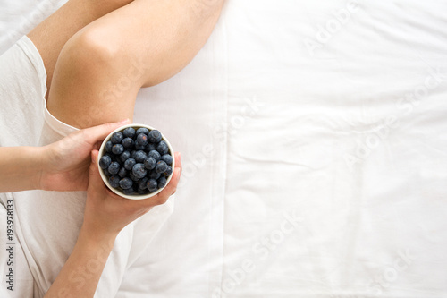Healthy eating concept. Woman having blueberries in bed. Top view.