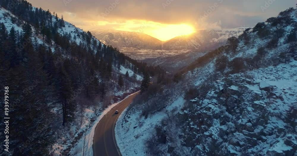 Aerial view car driving down snow covered winter road in canyon at sunset