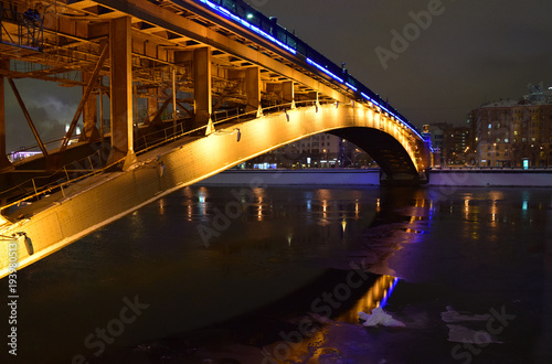Brightly illuminated bridge at night in winter. Reflections in the river. Moscow. Urban landscape.