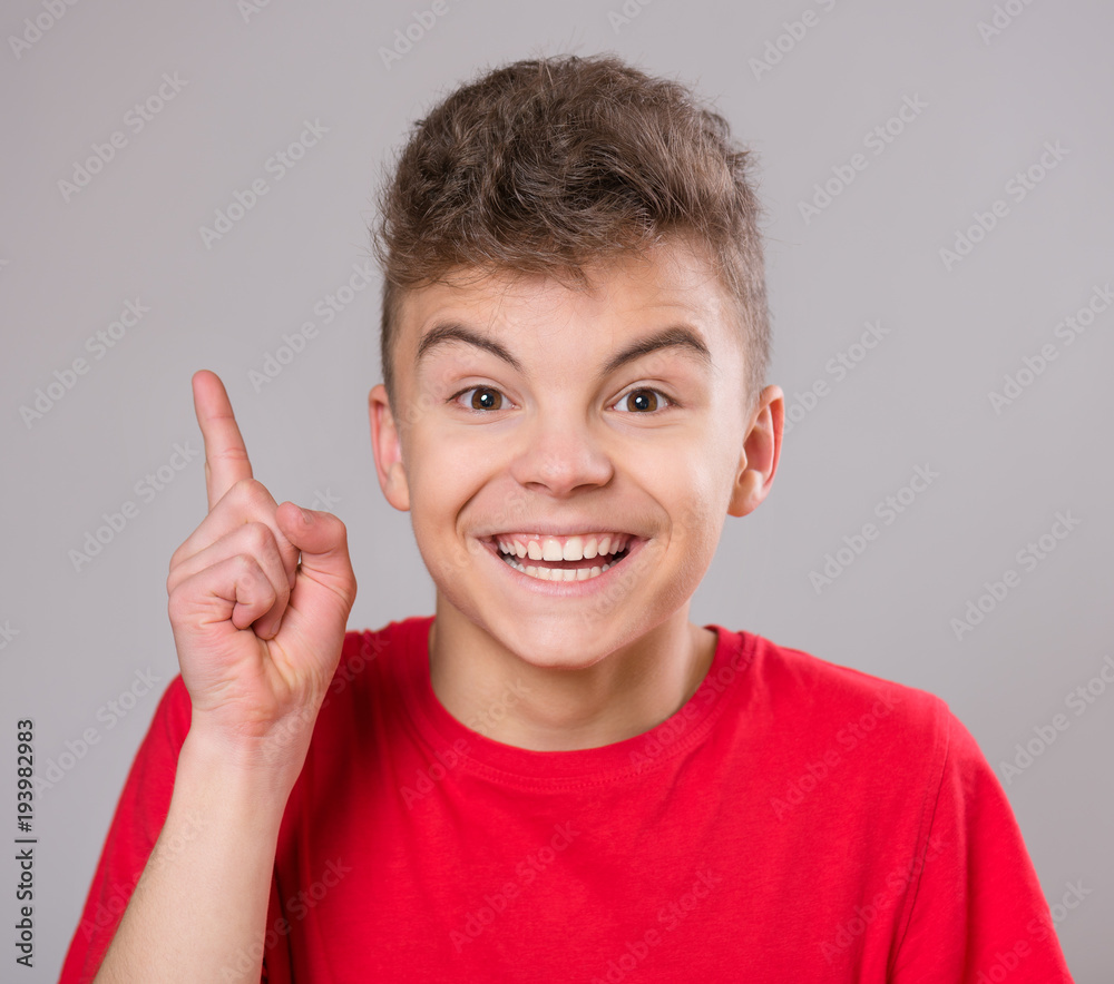 Emotional portrait of excited teen boy. Funny cute surprised child 14 year old looking at camera. Happy teenager pointing fingers up, on gray background. Emotional portrait of excited teen boy. Funny cute surprised child 14 year old looking at camera. Happy teenager pointing fingers up, on gray background.
