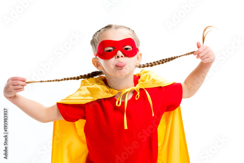 Little supergirl in yellow cape and red mask for eyes showing tongue and holding фототапет