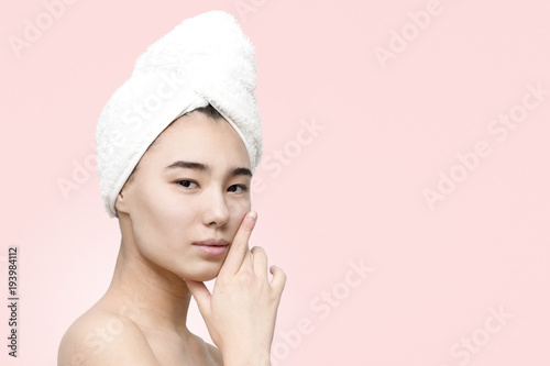 Close up portrait of pretty young asian woman with clean fresh skin after shower with towel on head on the rose background. Beauty, skincare, lifestyle concept