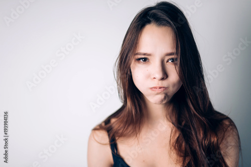 Indoor shot of cute girl, having doubtful and indecisive face expression, pursuing her lips as if forbidden to say anything.