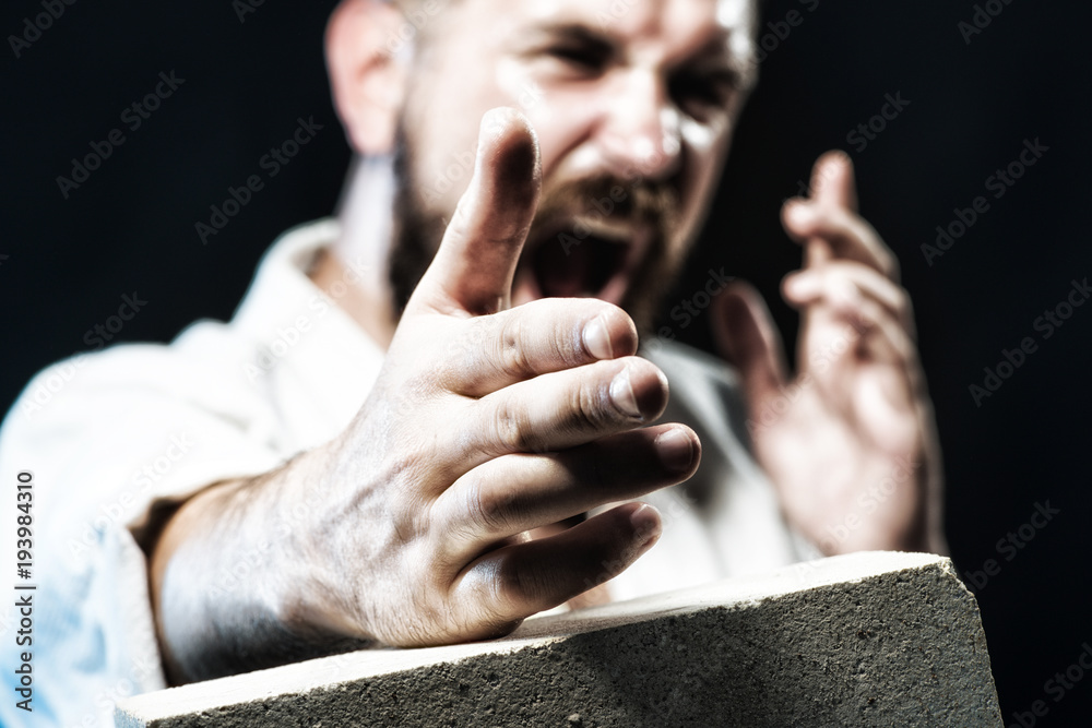 Strong, focused professional karate instructor training in judo, taekwondo, aikido. Karate man breaking with hand concrete brick. Karate man in action. MMA - Mixed martial art. Selective focus on hand