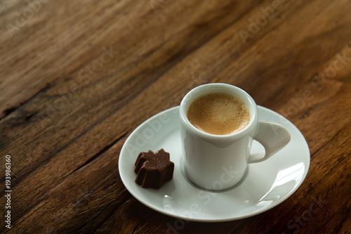 Fototapeta Naklejka Na Ścianę i Meble -  A cup of espresso with a chocolate candy maple leaf shaped on wooden background