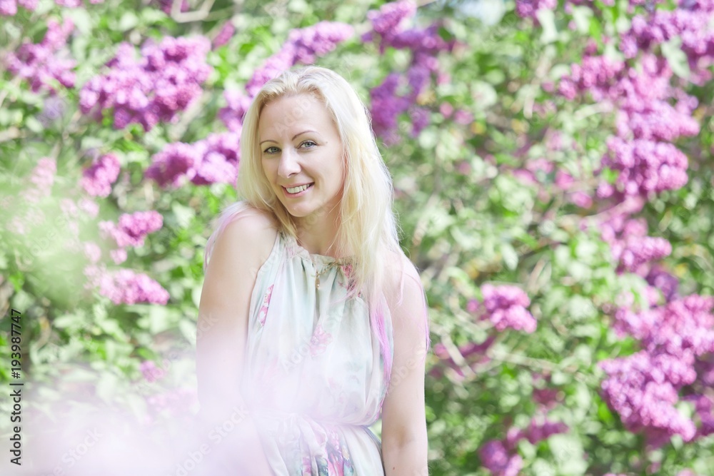 Young blonde woman standing in a spring blooming garden. Fashion Romantic girl outdoors portrait in blooming trees. Young blonde woman standing in a spring blooming garden. Fashion Romantic girl outdoors portrait in blooming trees.