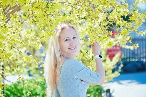 Young blonde woman standing in a spring blooming garden. Fashion Romantic girl outdoors portrait in blooming trees.