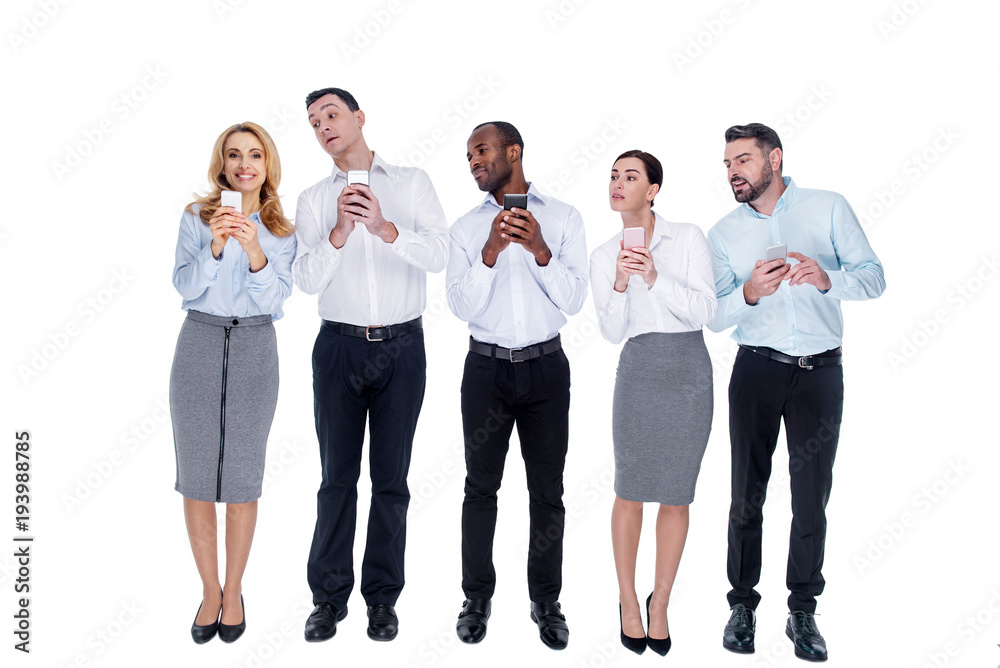 Obraz premium Show us. Beautiful inspired blond young woman smiling and standing with her phone and her colleagues trying to look at the screen of her phone