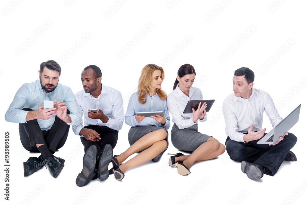 Working day. Good-looking alert stylish young co-workers smiling and working on their gadgets while sitting and interacting
