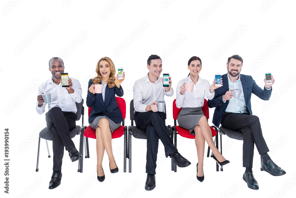 Relaxation. Attractive delighted stylish young co-workers smiling and drinking coffee and sitting on the chairs and holding their phones Relaxation. Attractive delighted stylish young co-workers smiling and drinking coffee and sitting on the chairs and holding their phones