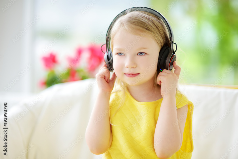 Cute little girl wearing huge wireless headphones. Pretty child listening to the music. Schoolgirl having fun listening to kid's songs at home. Cute little girl wearing huge wireless headphones. Pretty child listening to the music. Schoolgirl having fun listening to kid's songs at home.
