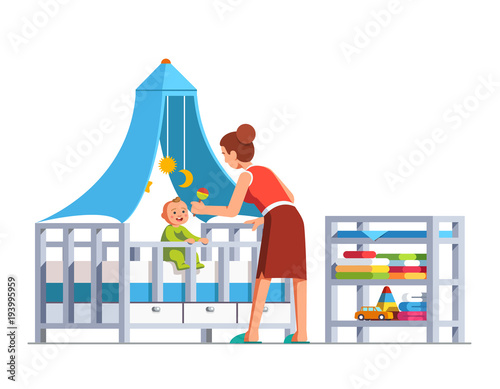 Mom playing rattle to baby son sitting in crib bed